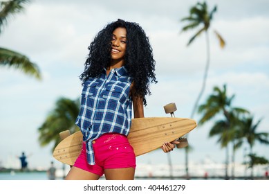 Smiling young woman portrait holding long board in South Pointe Park. South Beach Miami, Florida.