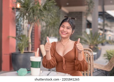 A Smiling Young Woman Poses For The Camera While Holding Two Thumbs Up Outside The Cafe.