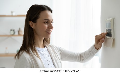 Smiling young woman pressing buttons on smart house system close up, standing at home, happy girl customer using air conditioning controller on wall, setting alarm password or comfort temperature - Shutterstock ID 1873196104