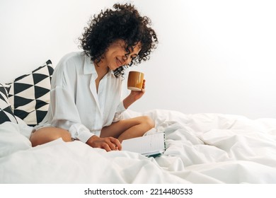 Smiling Young Woman Reading Journal Notes On Bed Drinking Some Tea. Copy Space.