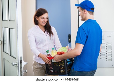 Smiling Young Woman Receiving Groceries From Delivery Man At Home