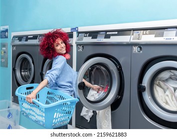 A Smiling Young Woman With Red Afro Hair Doing Laundry In A Blue Automatic Laundromat