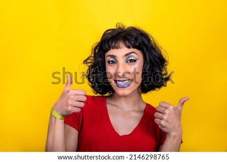 Smiling young woman in red t-shirt is showing thumbs up. Woman portrait with trendy look and bright colors on yellow background.