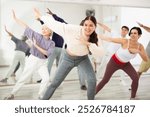 Smiling young woman rehearsing modern dance with group in dance school