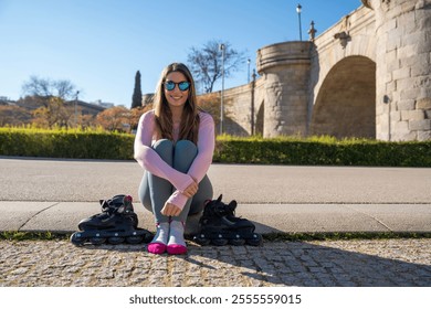 Smiling young woman resting after inline skating session in urban park with ancient bridge on background - Powered by Shutterstock