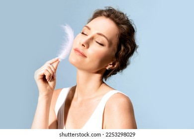 A smiling young woman runs a white feather across her smooth, delicate skin. Beautiful close-up portrait