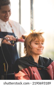 Smiling Young Woman Self Pampering Herself By Curling Hair With Machine By Professional Male Stylist In Modern Salon For A Hairdo And New Fashion Trend With Curling Treatment