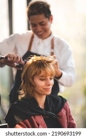 Smiling Young Woman Self Pampering Herself By Curling Hair With Machine By Professional Male Stylist In Modern Salon For A Hairdo And New Fashion Trend With Curling Treatment