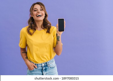 Smiling young woman showing blank screen smartphone isolated over blue background
