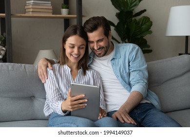 Smiling young woman showing funny photo video content in social network to husband, using digital computer tablet. Happy loving millennial family couple using modern technology gadget together at home - Powered by Shutterstock