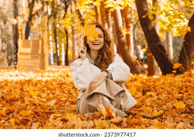 Smiling young woman sits in the autumn foliage on the ground of the forest with the yellow leaves - Powered by Shutterstock