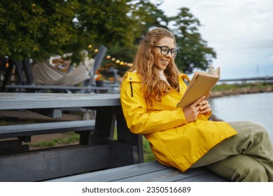 Smiling young woman sits on a bench and reads a book, enjoys the view of the lake. The concept of relaxation, enjoyment, solitude with nature. - Powered by Shutterstock