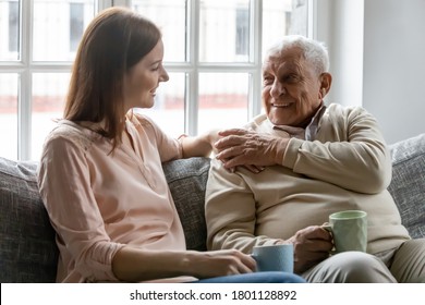 Smiling young woman sitting on sofa with happy older retired 70s father, enjoying pleasant conversation with cup of coffee tea together in living room, mature parents and grown children communication. - Powered by Shutterstock