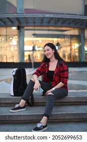 Smiling Young Woman Sitting On Stairs Of Shopping Mall At Night.