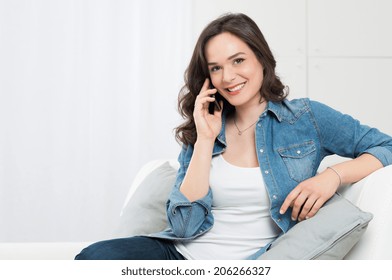Smiling Young Woman Sitting On Couch Talking On Phone