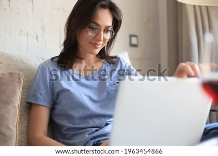 Smiling young woman sitting on sofa with laptop computer and chating with friends