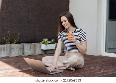 Smiling young woman sitting outdoor on terrace, working remotely online on laptop and drink fresh juice side view. Freelance, distant job, business lady. Working from home in summer time. - Shutterstock ID 2172069333
