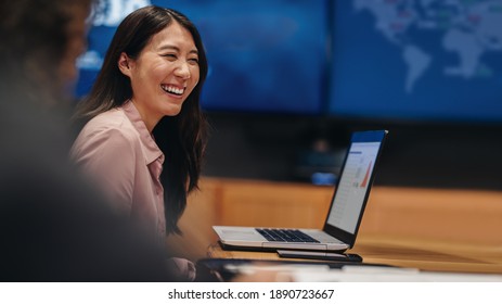 Smiling young woman sitting at table with laptop in meeting room. Businesswoman in meeting with team in office.