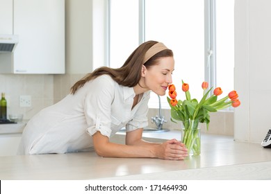 Smiling Young Woman Smelling Flowers In The Kitchen At Home