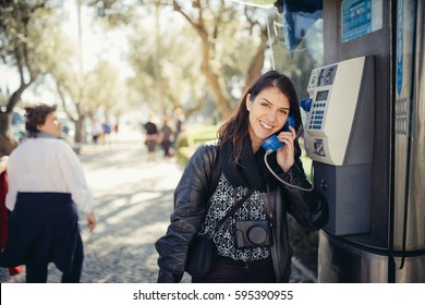 Smiling Young Woman Speaking On A Public Payphone Outside.Getting Information.Dialing Local Number In Foreign Country,low Cost Calls For International Dials.Coin Or Card Public Phone Used By Tourist