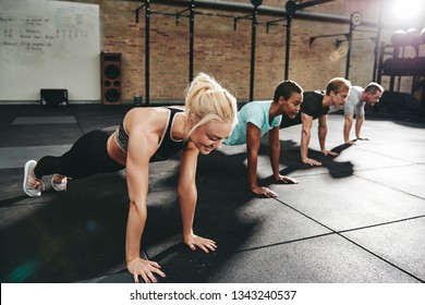 Smiling young woman in sportswear doing pushups at the gym with a group of friends during an exercise class