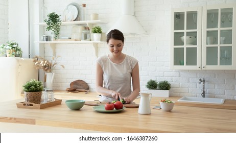 Smiling young woman stand at counter in white modern kitchen cooking healthy breakfast, happy millennial girl housewife preparing food meal, chop vegetables for salad in renovated design home - Powered by Shutterstock