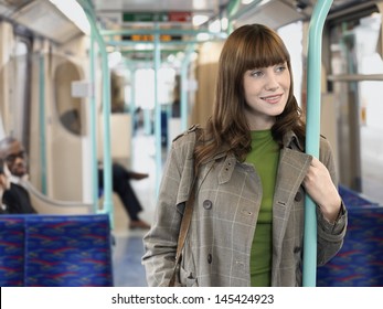 Smiling Young Woman Standing In Commuter Train Holding Bar