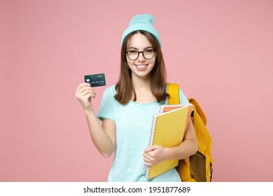 Smiling young woman student in casual blue t-shirt hat glasses backpack hold notebooks credit bank card isolated on pastel pink color background. Education in high school university college concept