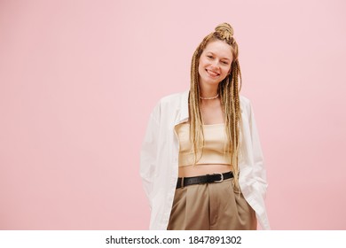 Smiling young woman with stylish blond afro braids over pink background. Posing for a photo, looking at the camera.