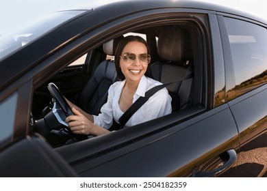 Smiling young woman in sunglasses with seatbelt driving car, view from outside - Powered by Shutterstock