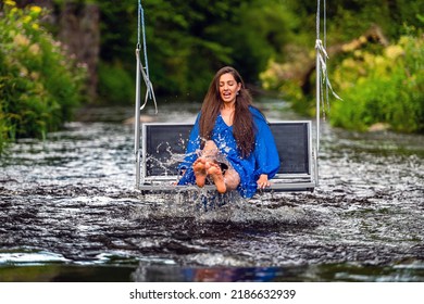 A Smiling Young Woman Swings On A Rope Swing Across A Fast-flowing River