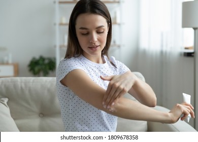 Smiling Young Woman Taking Care Of Herself, Moisturizing Elbow With Body Cream For Soft Skin. Happy Beautiful Lady Enjoying Home Spa Procedure, Applying Nourishing Organic Balm, Cosmetology Concept.