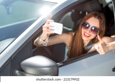 Smiling young woman taking selfie picture with smart phone camera outdoors in car - Powered by Shutterstock