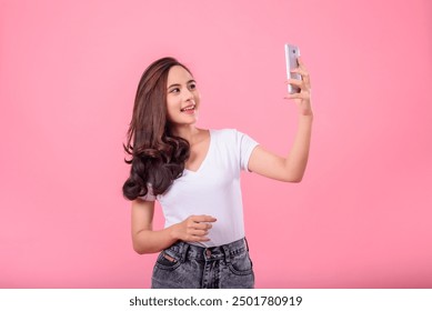 Smiling young woman is taking a selfie with her smartphone against a pink background - Powered by Shutterstock