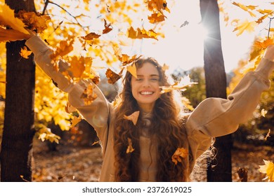 Smiling young woman throw up the autumn leaves in the forest at sunset - Powered by Shutterstock