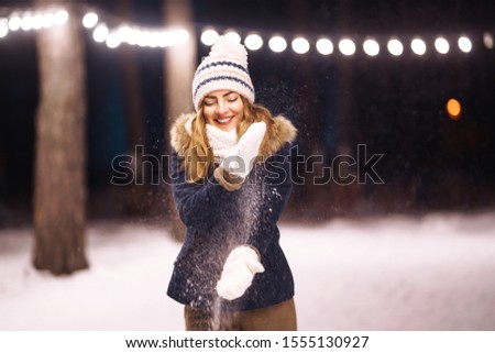Smiling young woman throwing snow in the air in the winter forest. Girl enjoys winter, frosty day. Playing with snow, a beautiful woman throws white, loose snow into the air. Fashion young woman.