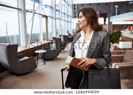 Smiling young woman with ticket and bag standing in departure lounge stock photo
