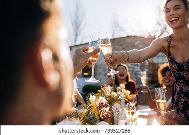 Smiling young woman toasting champagne with friend during an outdoor party. Young people enjoying at  party with focus on champagne glasses. - Powered by Shutterstock