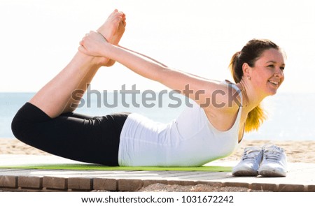 Smiling young woman training yoga poses sitting on beach in sunny morning