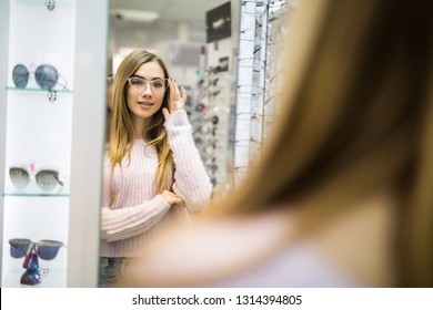 Smiling Young Woman Trying On Glasses On Mirror In Optician.