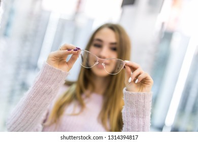 Smiling Young Woman Trying On Glasses On Mirror In Optician.