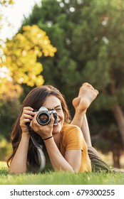 Smiling young woman using a camera to take photo at the park. - Shutterstock ID 679300255