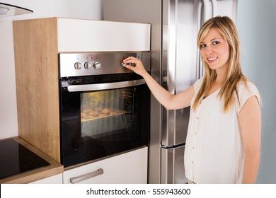 Smiling Young Woman Using Oven For Baking Cookies In Kitchen