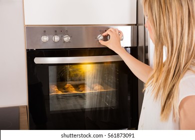 Smiling Young Woman Using Oven For Baking Cookies In Kitchen