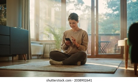 Smiling Young Woman Using Smartphone at Home, does Remote Work. Beautiful Girl Sitting on the Floor Uses Mobile Phone Internet, e-Shopping, Order Products Online, Post on Social Media. Sunny Home - Powered by Shutterstock