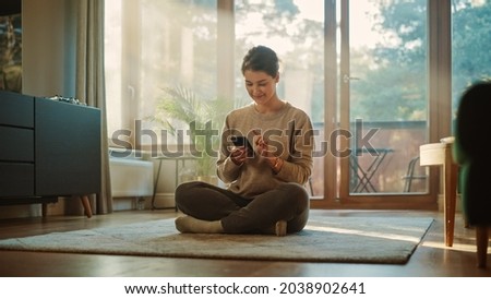 Smiling Young Woman Using Smartphone at Home, does Remote Work. Beautiful Girl Sitting on the Floor Uses Mobile Phone Internet, e-Shopping, Order Products Online, Post on Social Media. Sunny Home Photo stock © 