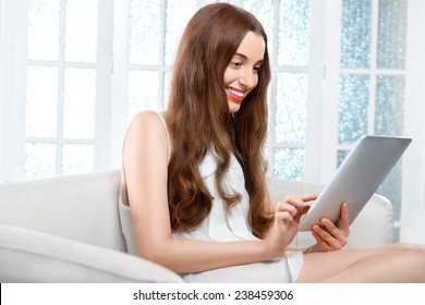 Smiling young woman using tablet sitting on the couch at home