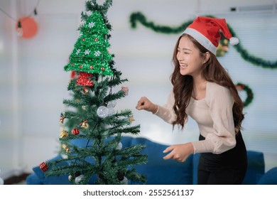 Smiling young woman wearing santa hat decorating christmas tree with colorful ornaments and lights, enjoying festive holiday season at home - Powered by Shutterstock