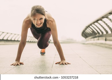 Smiling Young Woman Wearing Sportswear, Looking At Camera And Doing Mountain Climber Exercise. Front View.