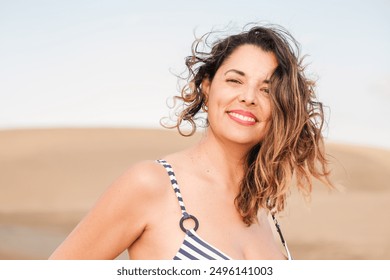 Smiling young woman wearing a striped bikini with the dunes behind in a tourist destination - Powered by Shutterstock